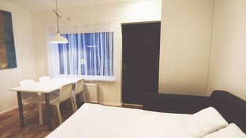 A room with a bed, a table with chairs, a window with curtains, and a door.