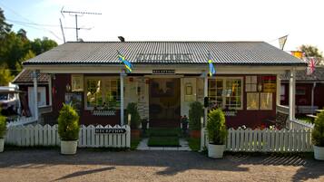 En receptionsbyggnad med ett vågformat metalltak, ett vitt staket och krukväxter vid ingången.