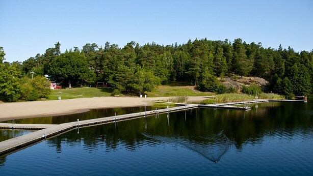 Un lac paisible, avec une jetée en bois qui s’avance sur l’eau, entouré d’une forêt dense et bordé d’une plage de sable.