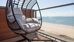 Una silla de mimbre con cojines junto a un ventanal con vistas a la playa.
