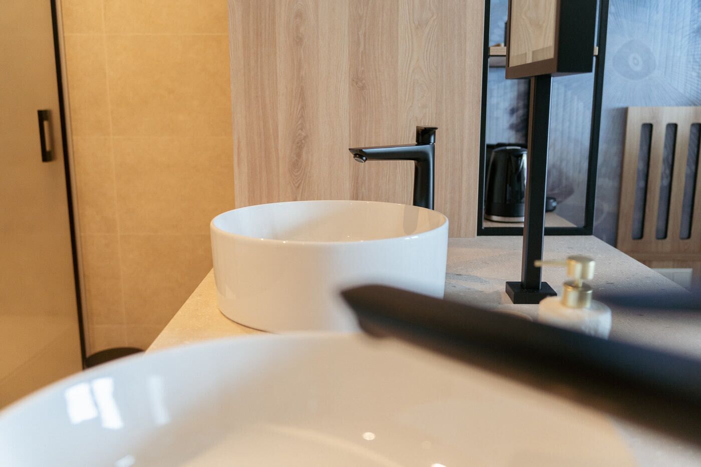 A modern bathroom with a white sink, a black faucet, and a wooden door.