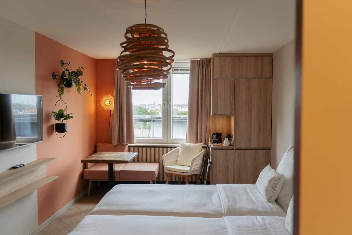 A hotel room with a bed, a desk, a chair, a TV, and a window with a view of the city.