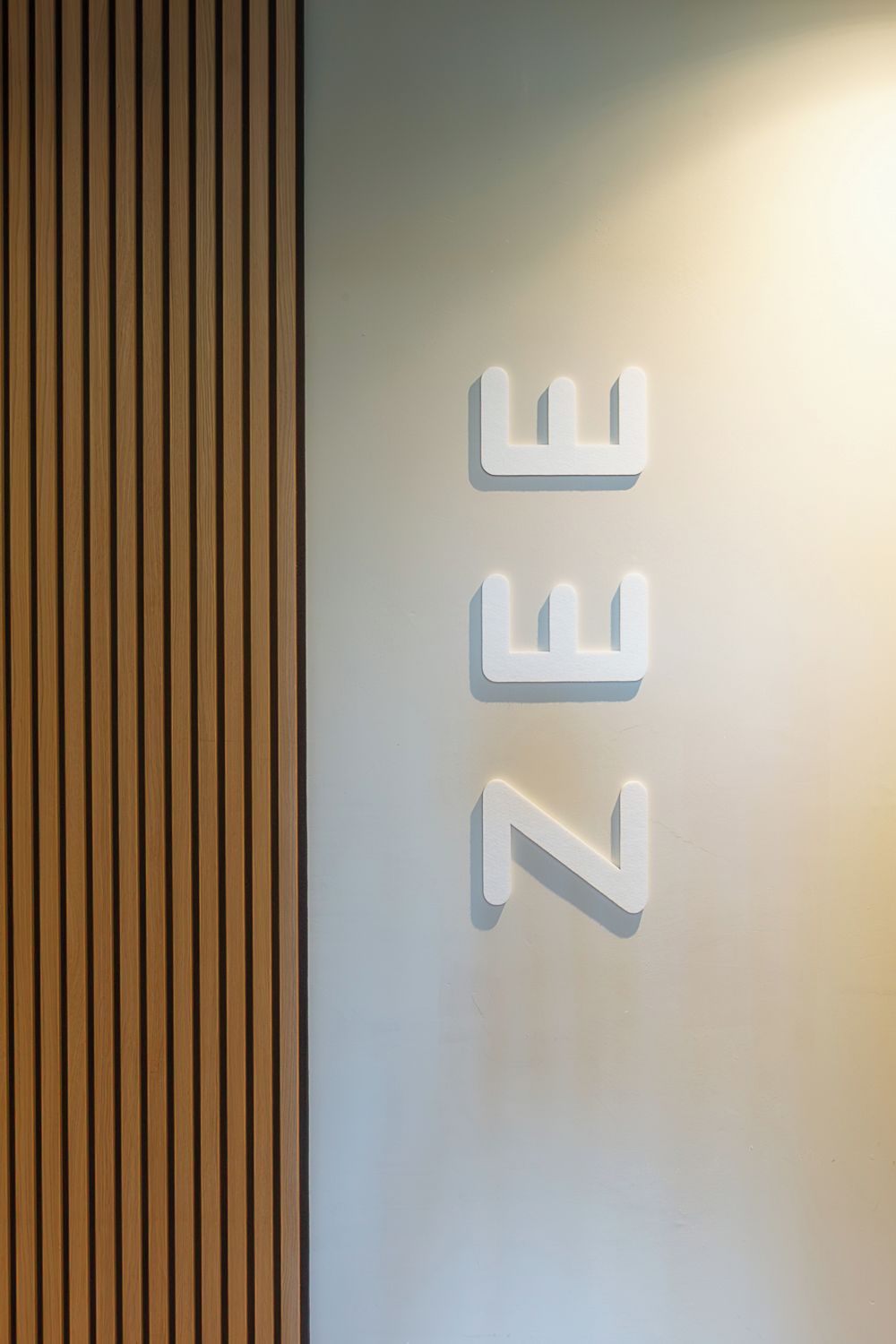 A wall with vertical wooden slats and a white illuminated sign with the letters "ZEE".