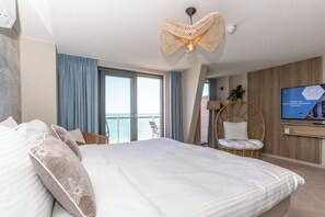 A hotel room with a large bed, a television, a wicker chair, and a view of the sea. - Beachfront Boutiquehotel (Vlissingen)