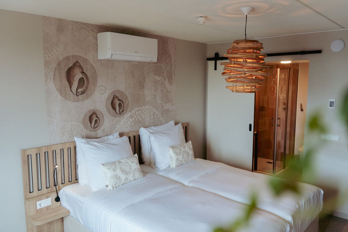 A bedroom with a bed, a wooden headboard, a wall-mounted air conditioner, and a hanging light fixture.