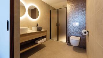 Een moderne badkamer met een houten wastafelmeubel, een ronde spiegel, een toilet en een douchehoek.