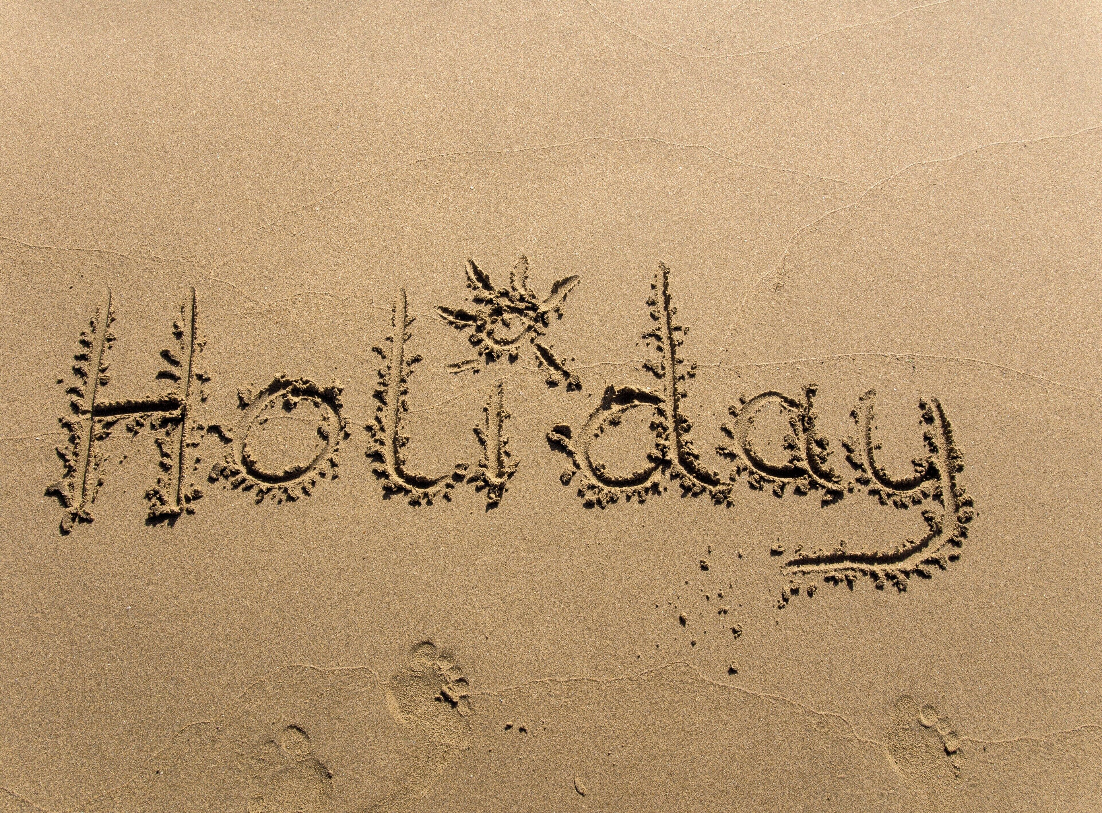 Het woord 'Holiday' in het zand geschreven.