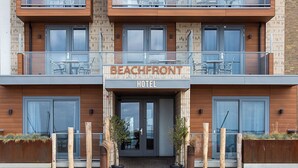 Un hotel de varios pisos con fachada de madera, balcones con mobiliario exterior y un letrero que dice "BEACHFRONT HOTEL".