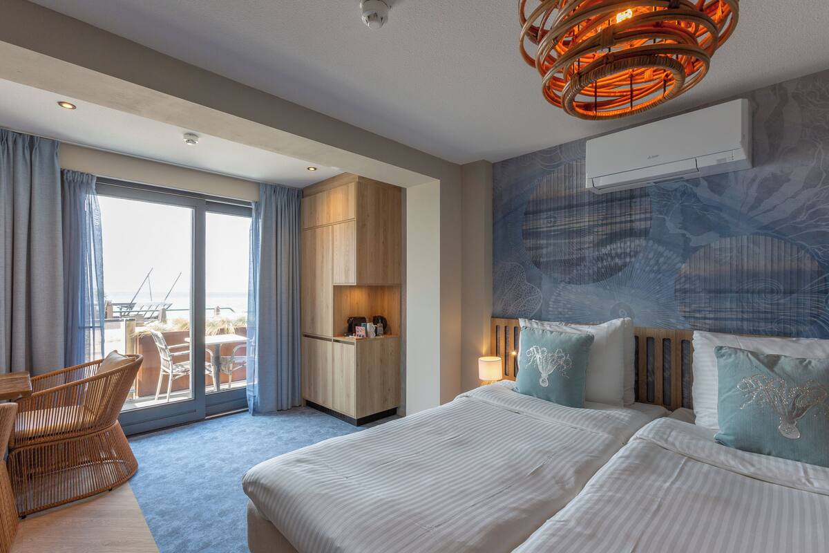 A hotel room with a large bed, a seating area with a chair, a desk, and a view of the outdoors through a sliding door.
