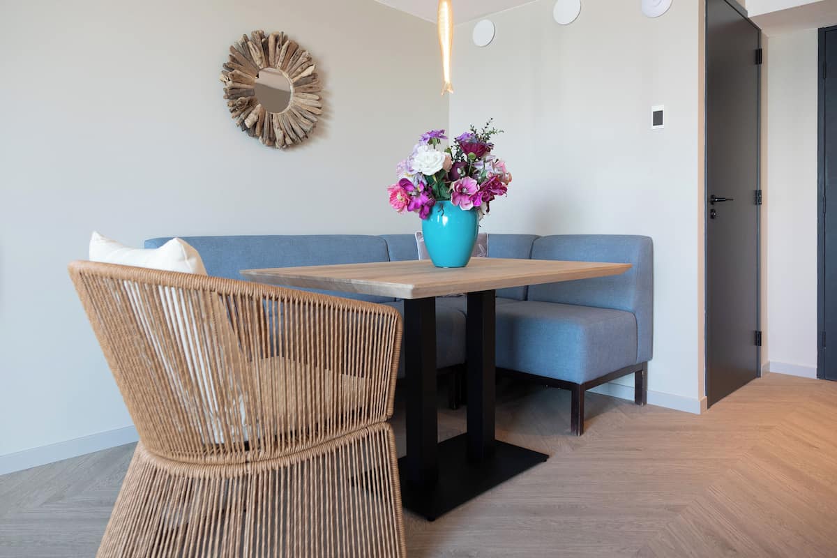 A room with a wooden table, a blue sofa, and a wicker chair. There is a vase with flowers on the table.