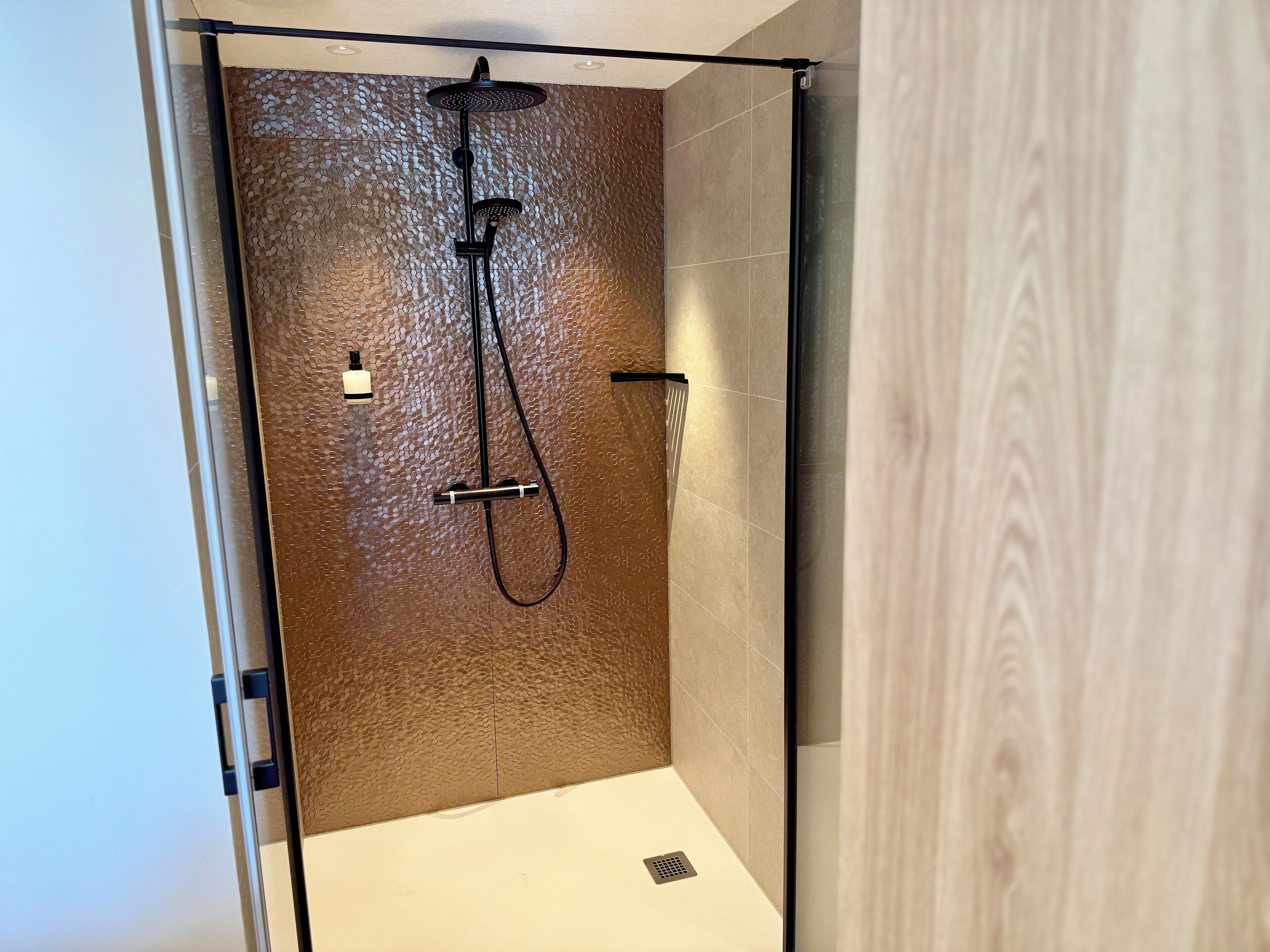 Un espacio de ducha moderno con pared texturizada, un cabezal de ducha de mano y un grifo empotrado.