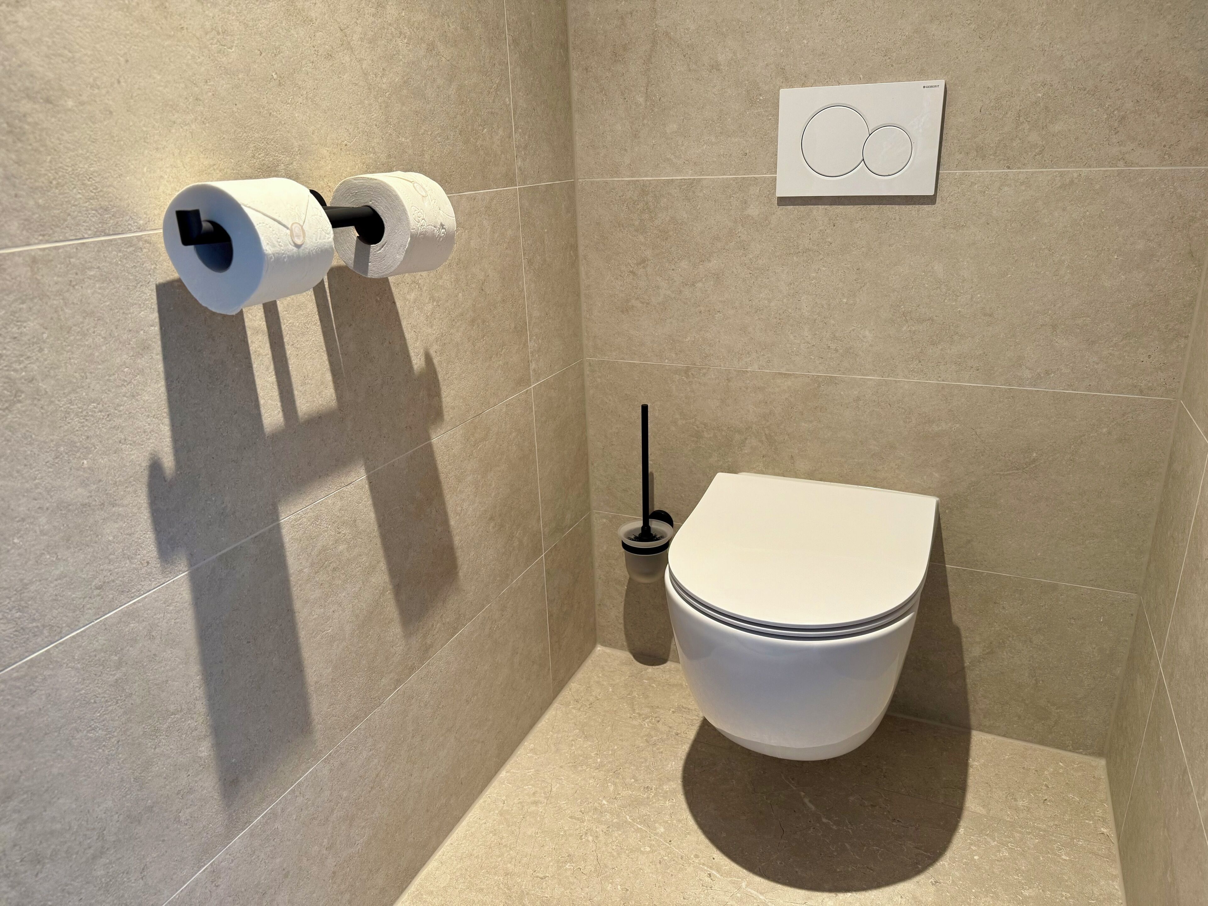 Un baño moderno con inodoro, dispensador de papel higiénico y secamanos.