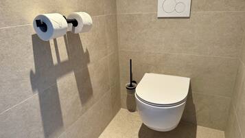 Un baño moderno con inodoro, dispensador de papel higiénico y secamanos.