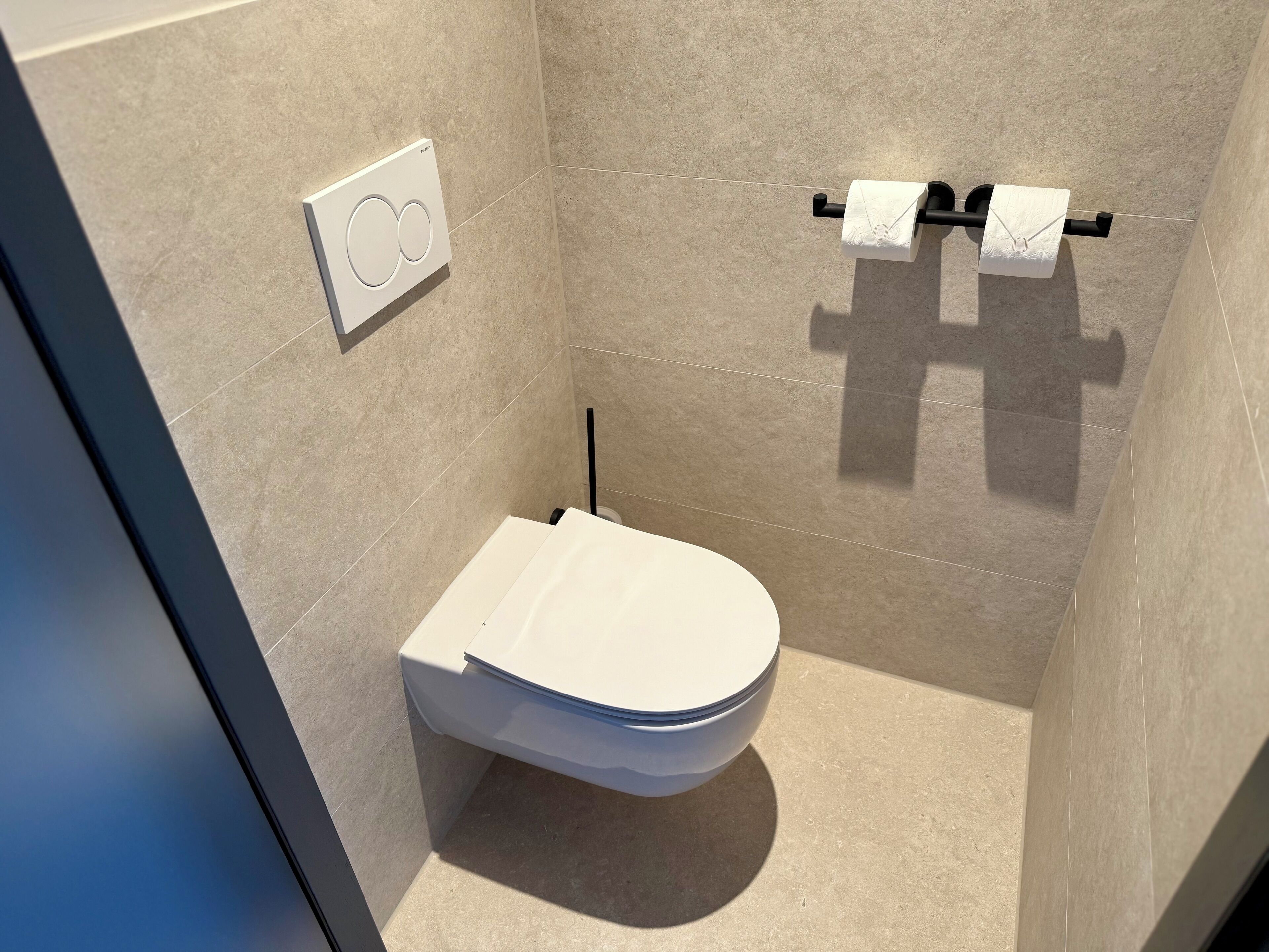Ein modernes Badezimmer mit Toilette, Handtuchspender und Toilettenpapierhalter.
