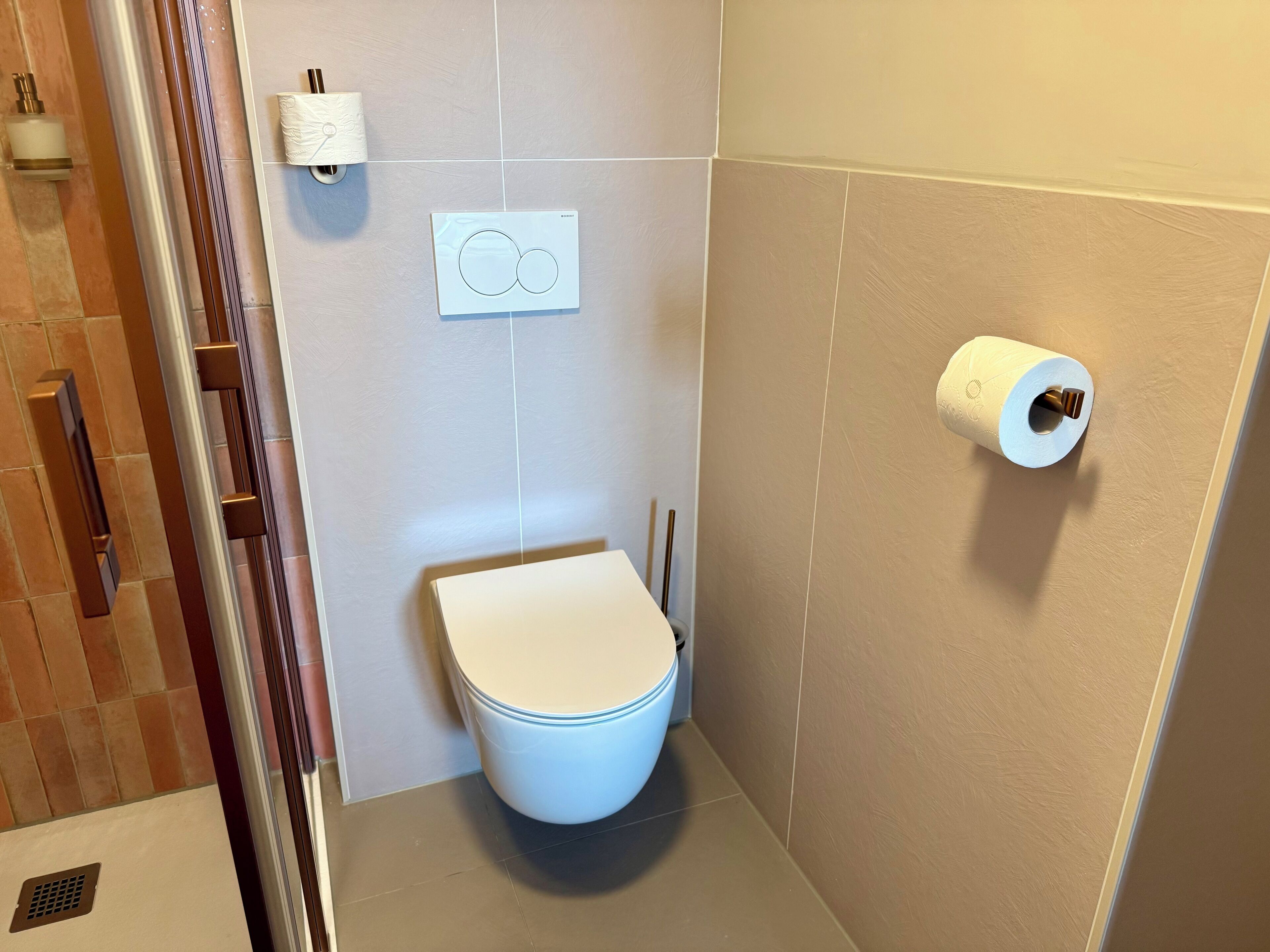 Un baño con un inodoro, un dispensador de toallas de papel y un porta papel higiénico en la pared.