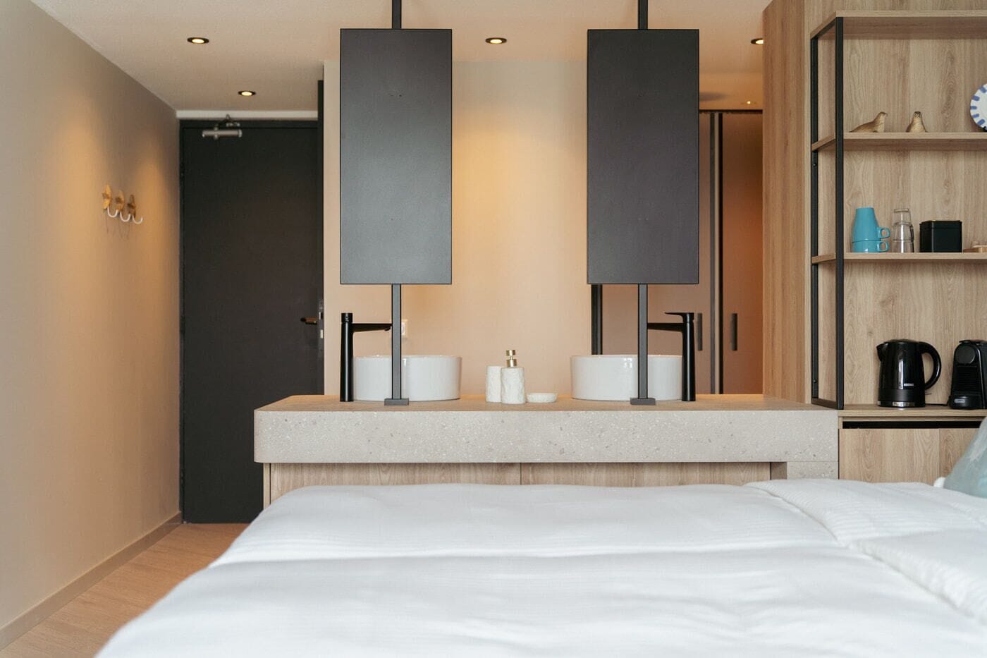 Una moderna camera d'hotel con un letto grande, una scrivania integrata con un lavandino e un'armadio in legno.