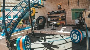 A gym with weightlifting equipment, a tire rack, and a brick wall with a clock. - pousada sal e mar (ipojuca)