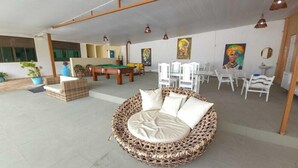 A spacious indoor area with a pool table, a round wicker sofa, and white chairs. - pousada sal e mar (ipojuca)