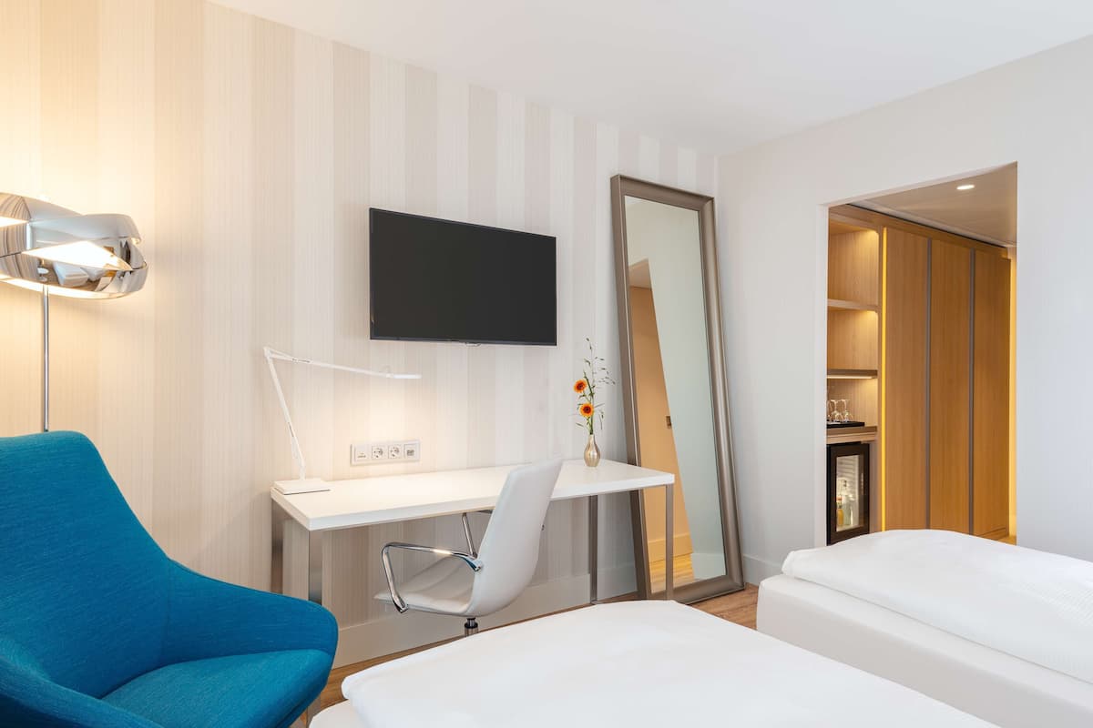 A modern hotel room with a bed, a desk with a chair, a TV, and a large mirror.