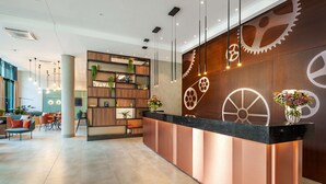 Un espace d’accueil moderne avec un comptoir en bois, des étagères ornées de plantes et un grand mur décoré de motifs représentant des engrenages.