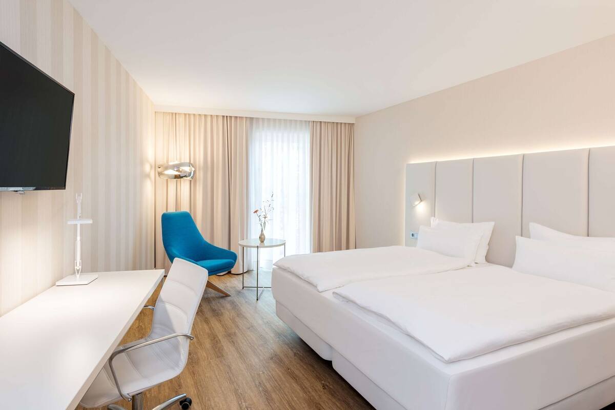 A hotel room with a bed, a desk, a chair, a TV, and a lamp.