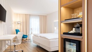 Une chambre d’hôtel équipée d’un lit, d’un bureau, d’une chaise, d’un minibar et d’une télévision.