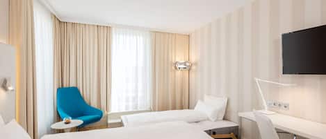 A hotel room with two beds, a desk, a chair, a TV, and a window with curtains.