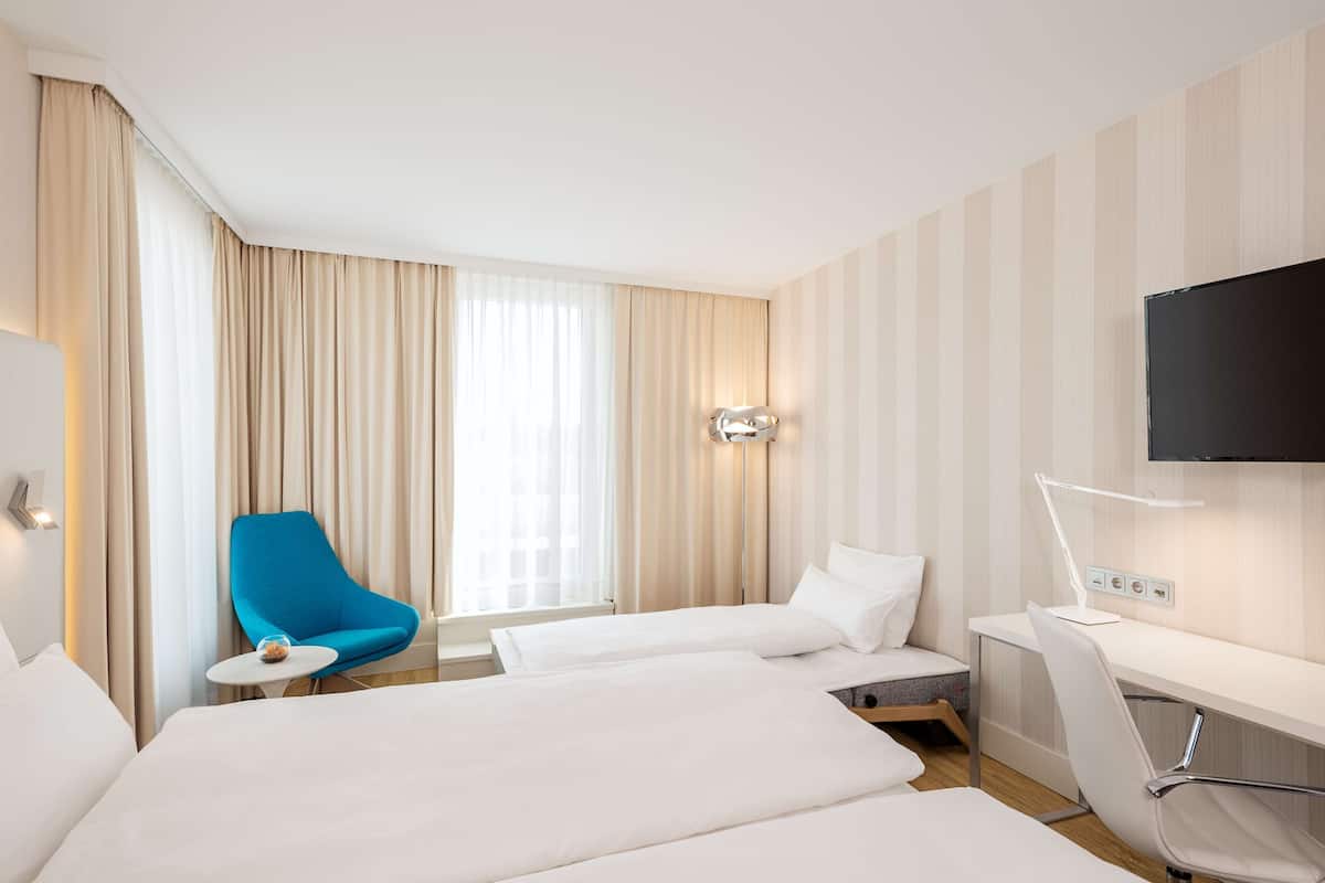 A hotel room with two beds, a desk, a chair, a TV, and a window with curtains.