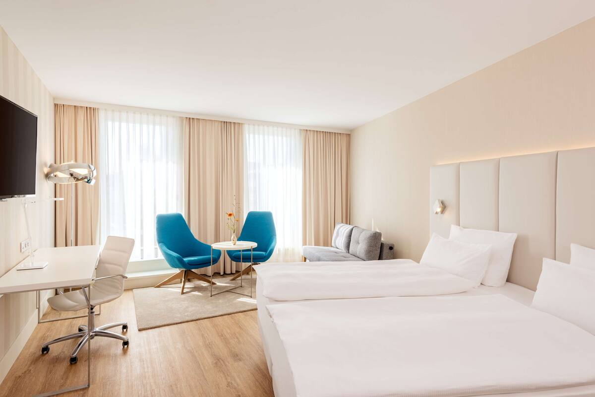 A hotel room with a desk, two chairs, a bed, and a TV.