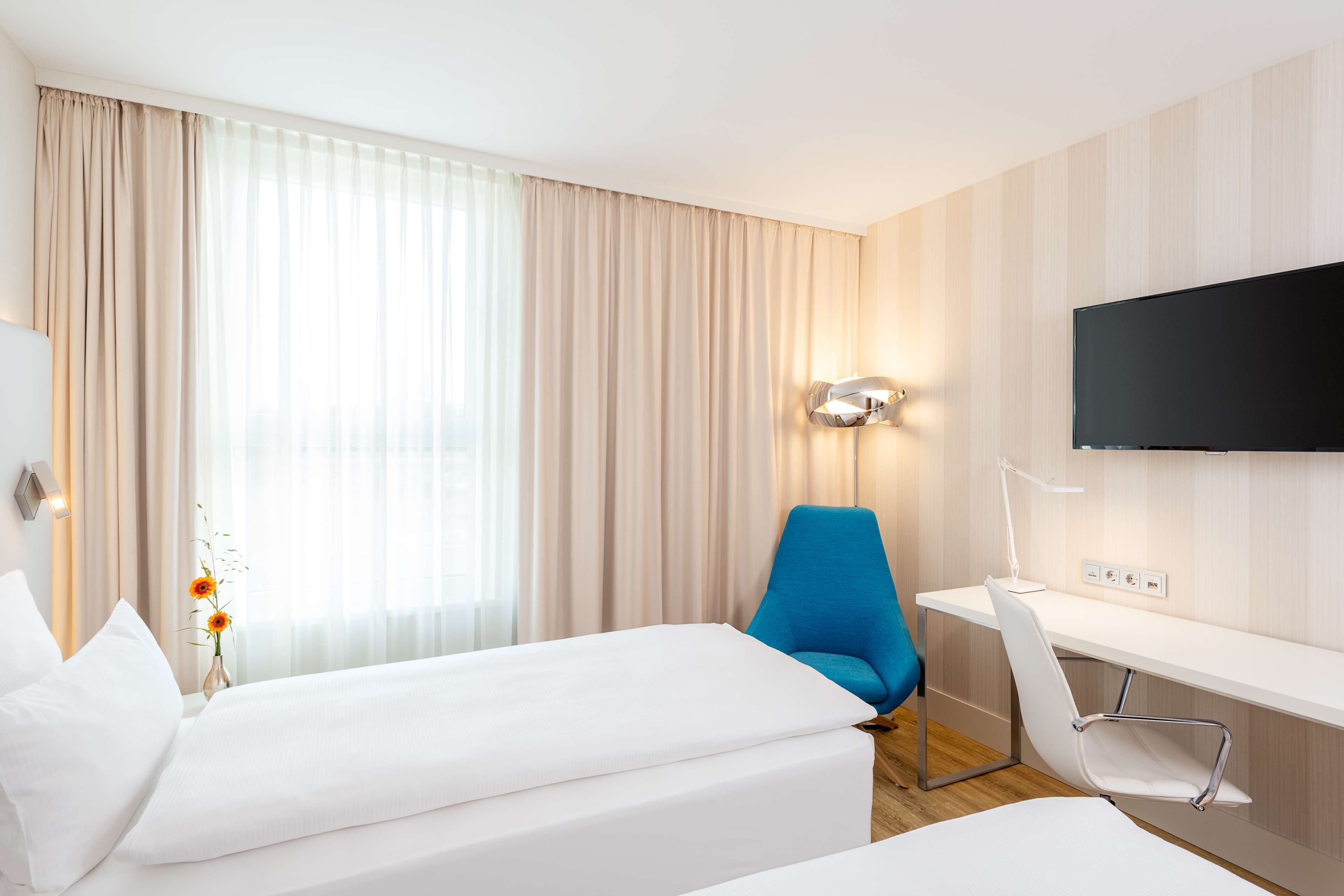 A hotel room with two beds, a desk, a chair, a TV, and a window with curtains.
