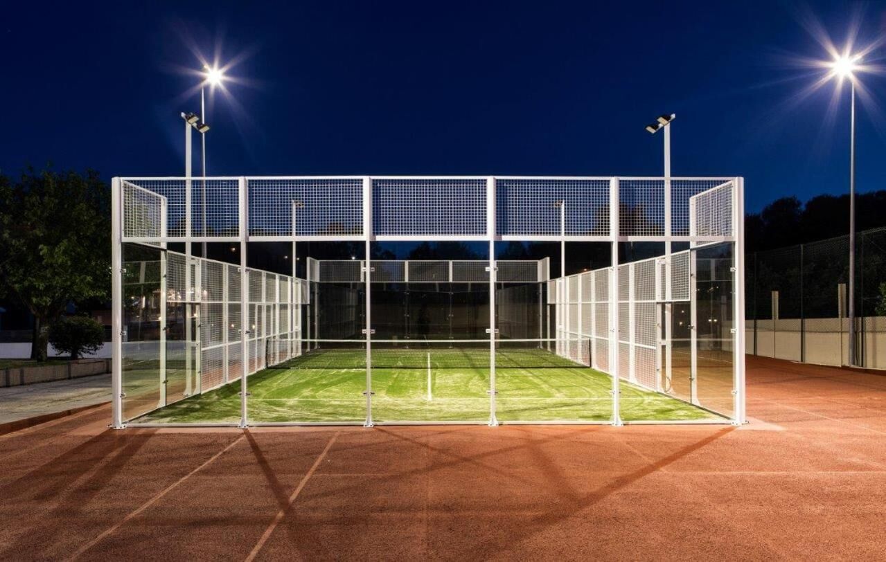 Una cancha deportiva con cerramiento de red y césped artificial, rodeada de una superficie roja.