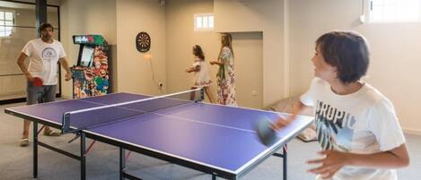A ping pong table in a room with a dartboard and a colorful arcade machine.