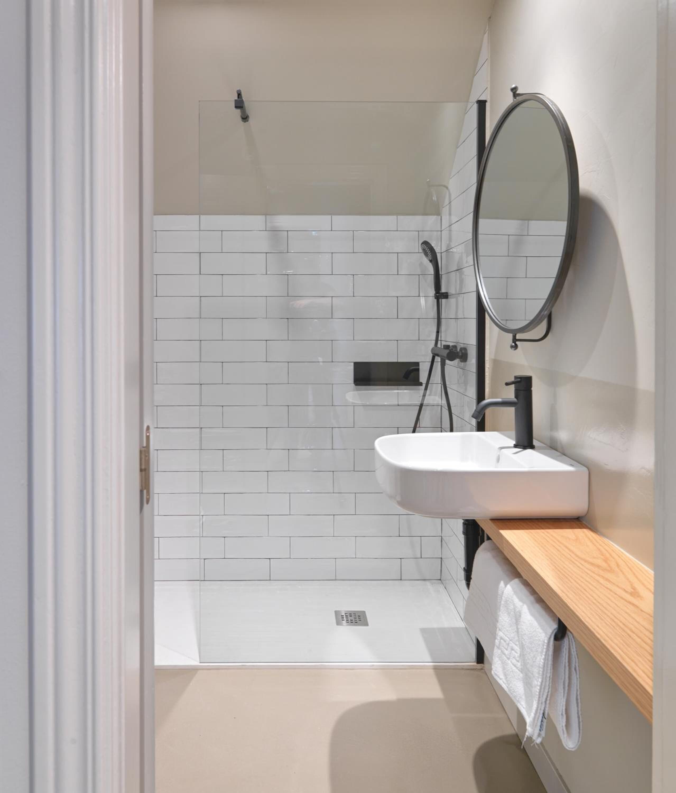 Un baño moderno con ducha de azulejos blancos, lavamanos con espejo y tocador de madera.