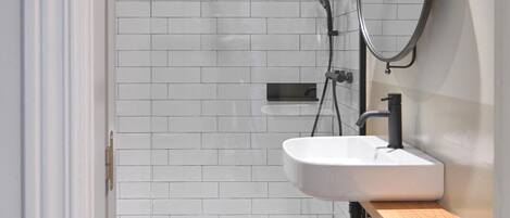 Un baño moderno con ducha de azulejos blancos, lavamanos con espejo y tocador de madera.