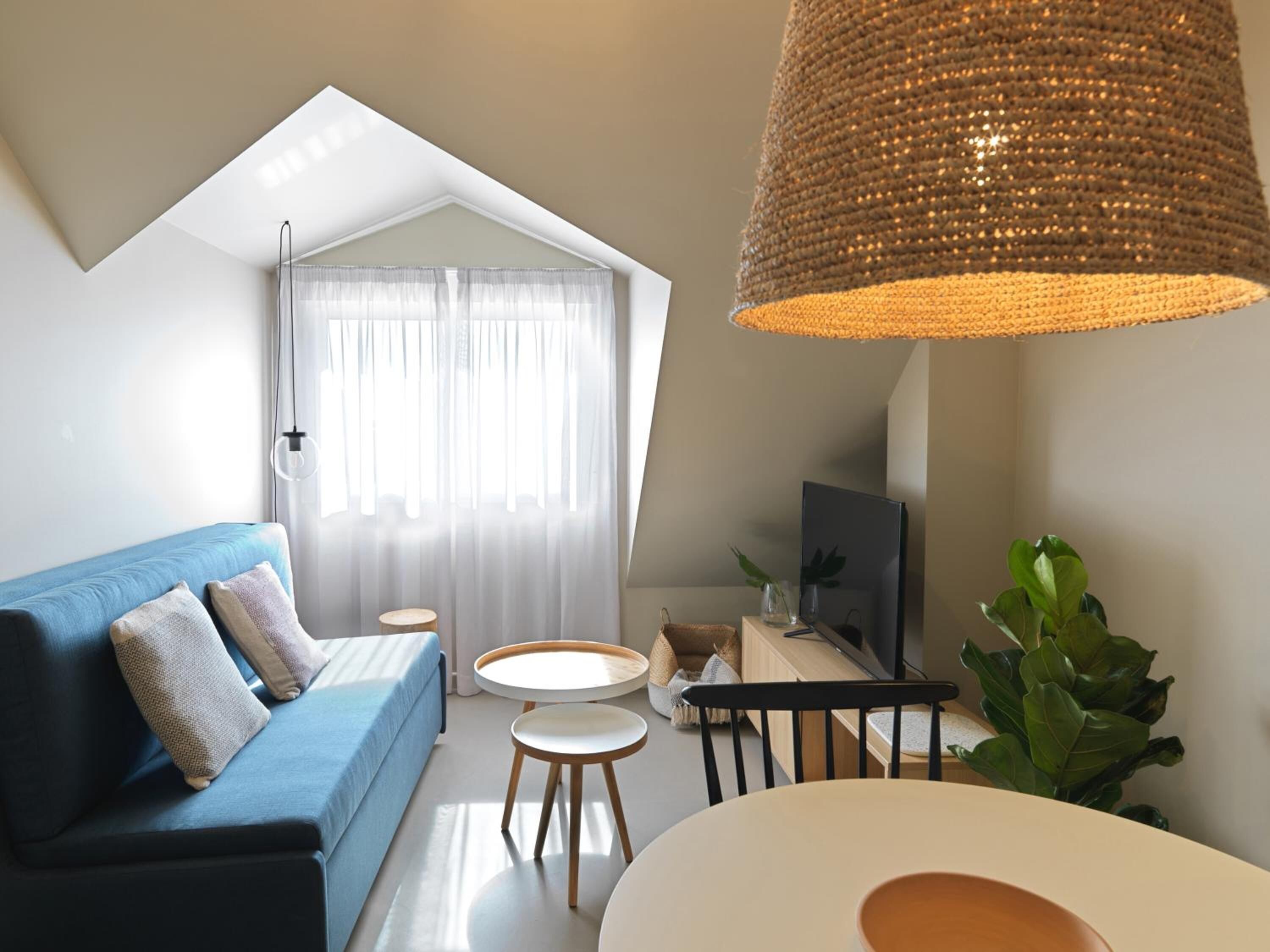 Un salón moderno con un sofá azul, una mesa redonda, un televisor y una lámpara colgante grande de tejido.