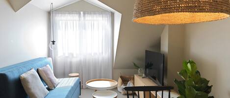 Un salón moderno con un sofá azul, una mesa redonda, un televisor y una lámpara colgante grande de tejido.