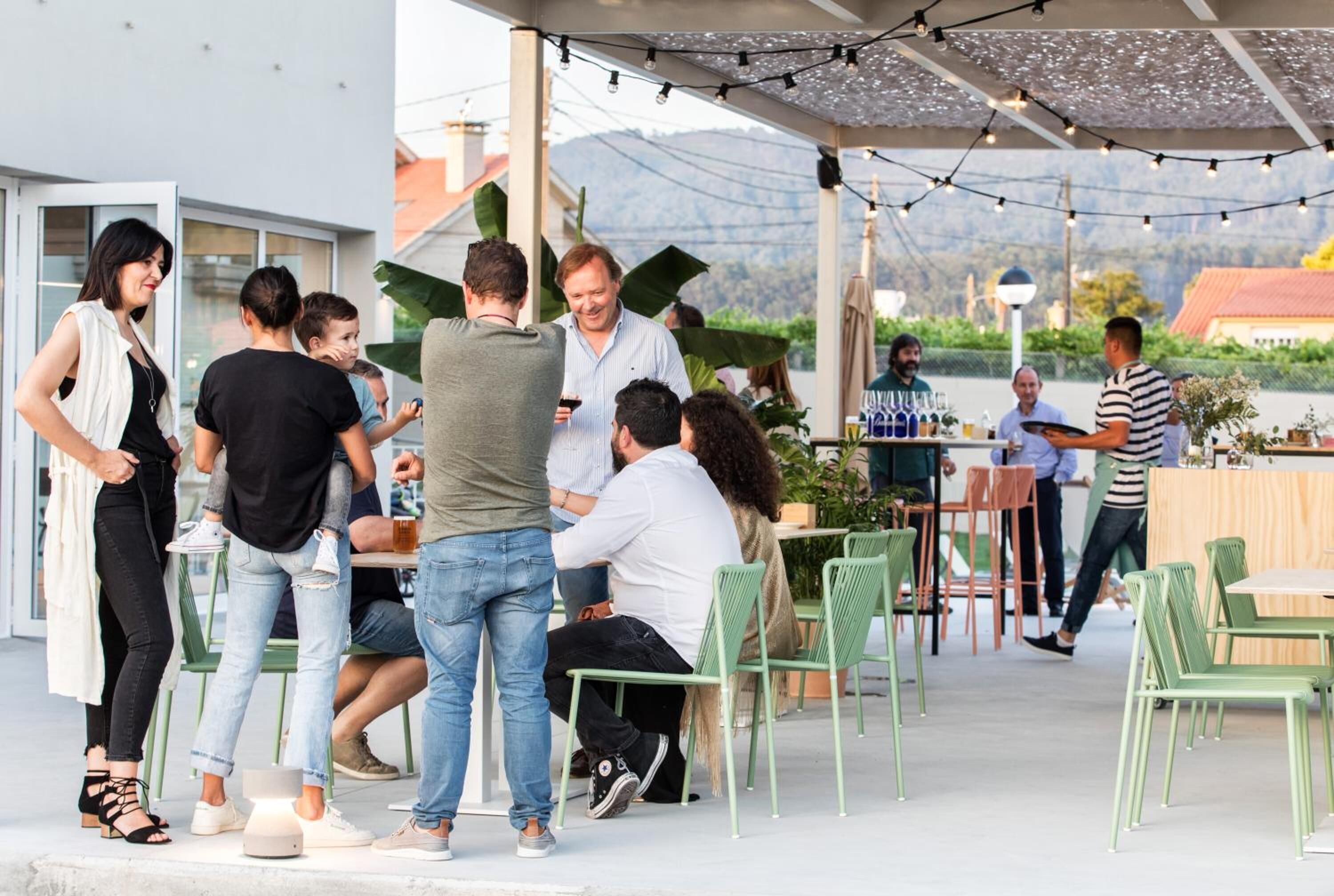 Ein Terrassenbereich im Freien mit grünen Stühlen und Tischen, umgeben von einer Überdachung mit Lichterketten.
