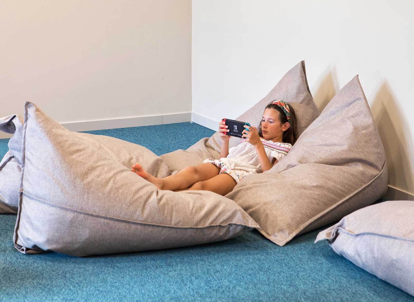 A child lying on a bean bag chair in a room with a blue carpet and white walls.