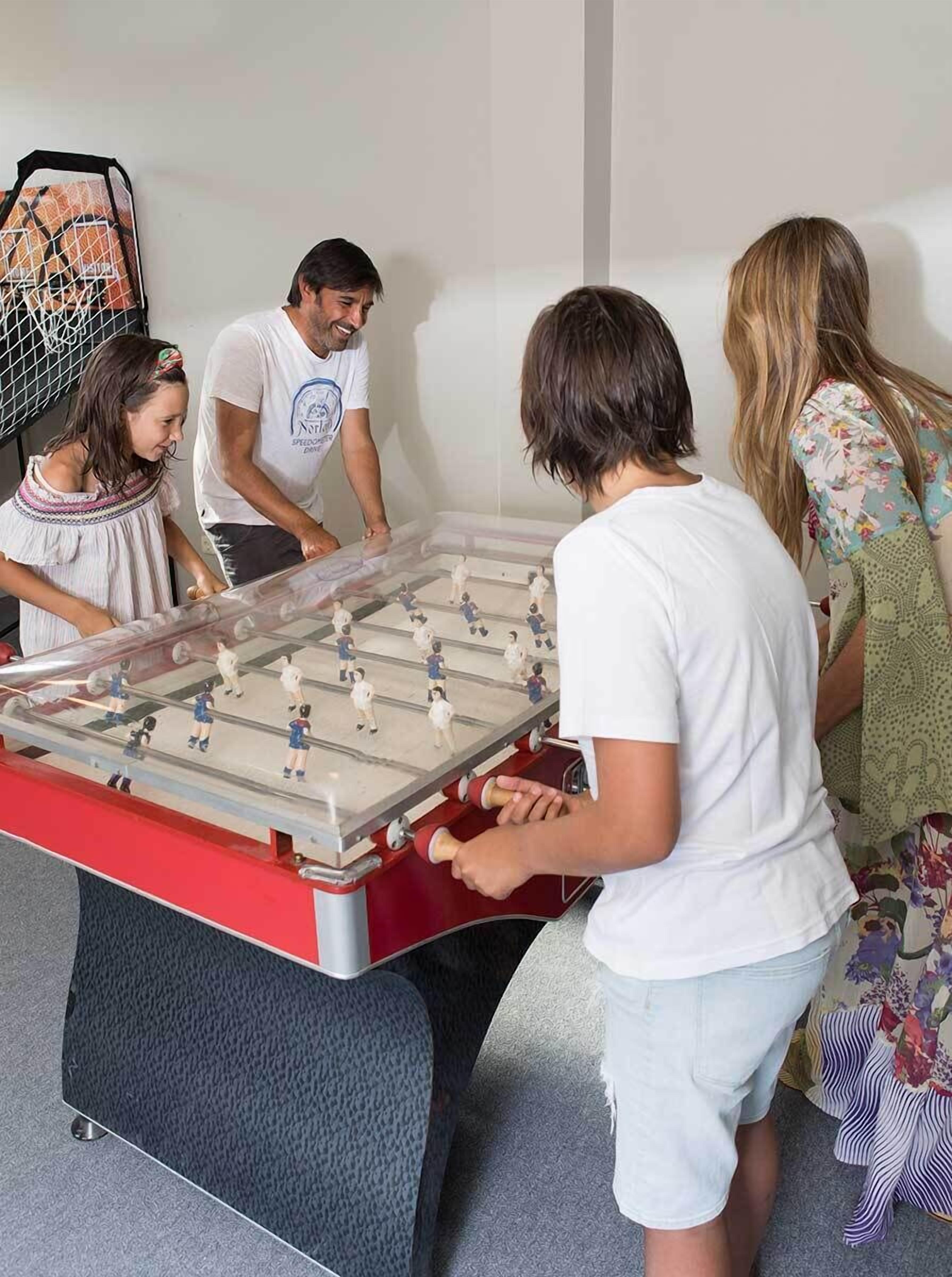 A foosball table in a room with a plain wall and a basketball hoop in the background.