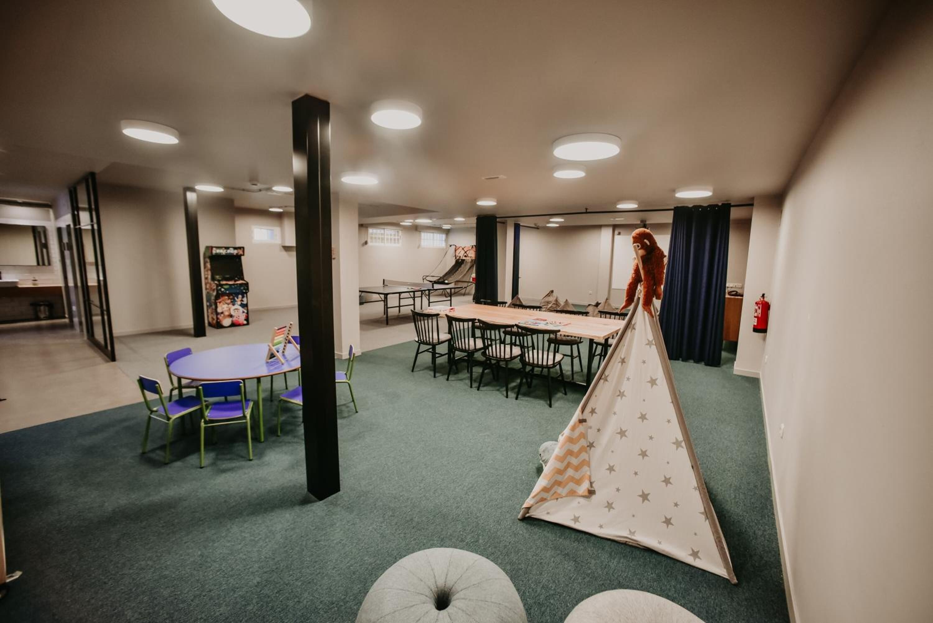 A room with a long table, chairs, a tent, and a basketball hoop.