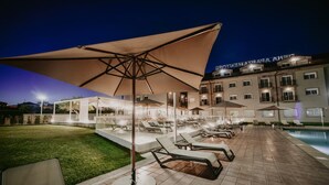 A hotel pool area with sun loungers and umbrellas, a well-lit lawn, and a building with illuminated signage. - Apartamentos Dena (Meano)