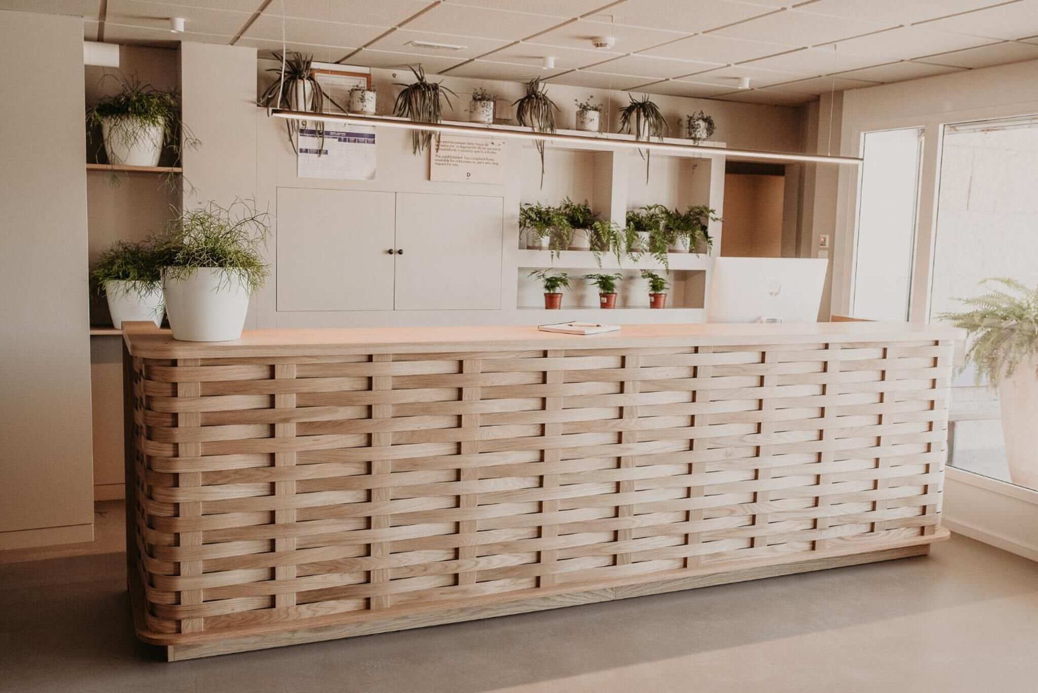 Een receptiebalie met een houten lattenstructuur, kamerplanten op planken, en een prikbord.