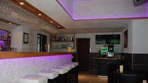 A bar area with a white brick wall, bar stools, and a counter with a purple light. There are shelves with bottles and glasses, and a chalkboard menu on the wall. - Hotel Winzerhaus Gaertner an der Loreley (Sankt Goar)