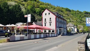 A hotel with a red awning, a sign indicating a restaurant, and a view of a mountain. - Hotel Winzerhaus Gaertner an der Loreley (Sankt Goar)