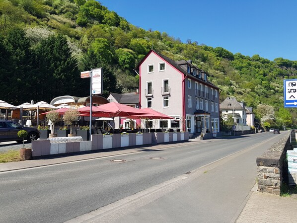 Un hôtel avec un auvent rouge, une enseigne indiquant la présence d’un restaurant et une vue sur une montagne.