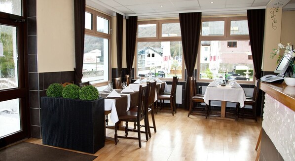 A restaurant with multiple tables, dark wooden chairs, and a black planter with green plants.
