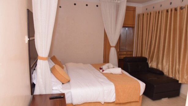 Una habitación de hotel con cama, una silla, televisor y cortinas.
