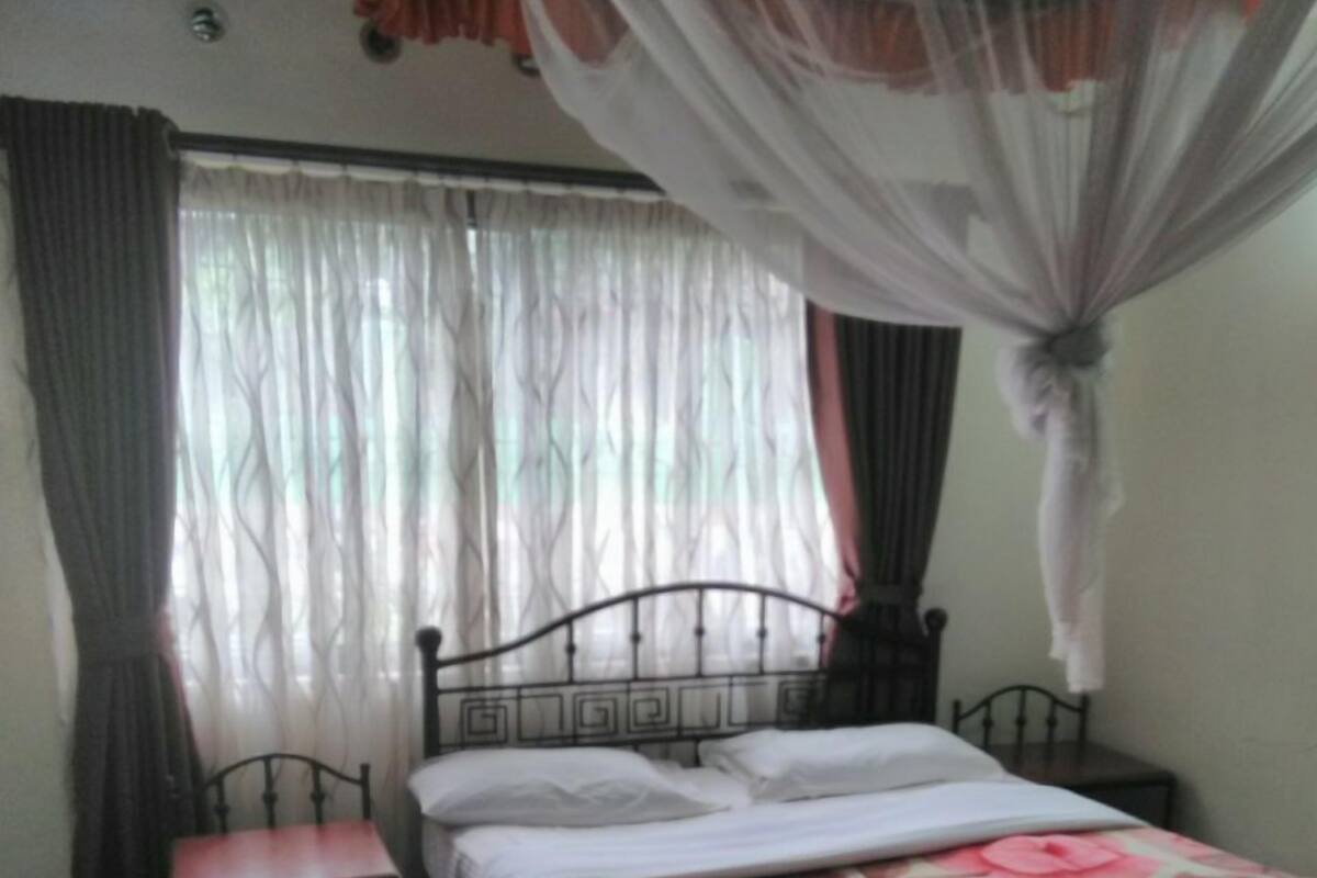 Un dormitorio con cama, mesita de noche, silla y ventana con cortinas.