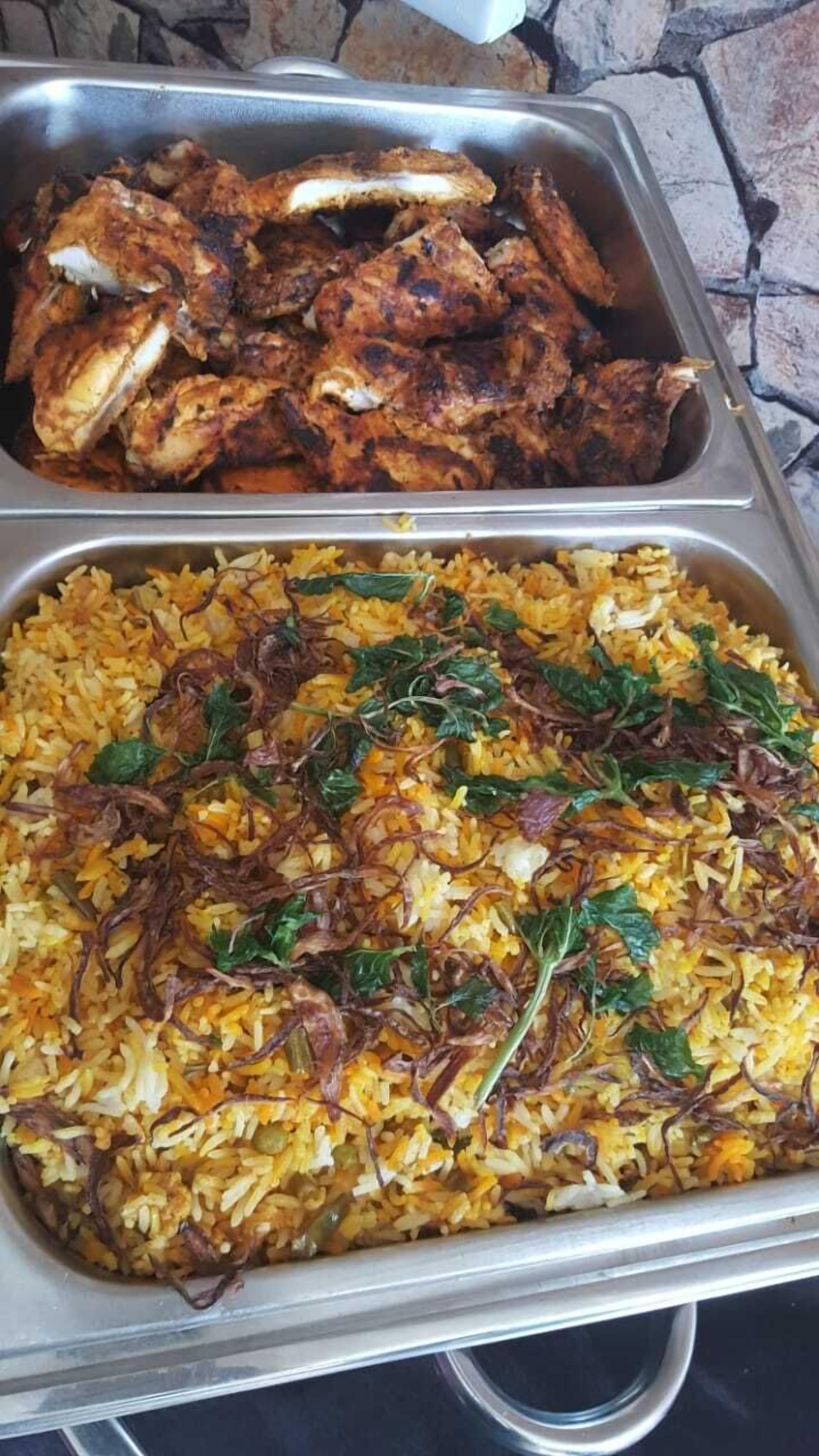 Un buffet proposant du poulet grillé et un plat de riz garni d’herbes aromatiques.