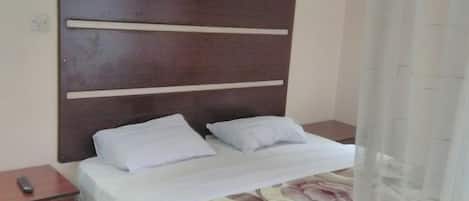 A hotel room with a bed, a nightstand, and a curtain.